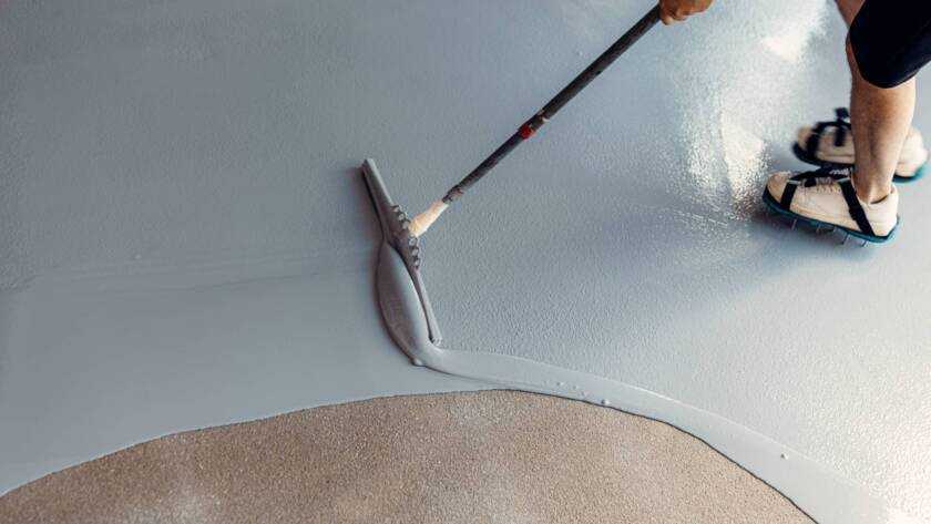 A construction worker apply grey epoxy resin in an industrial hall