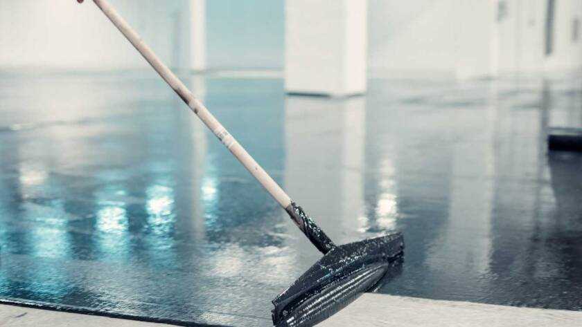 Worker applies gray epoxy reisin to a new floor. Modern Surface